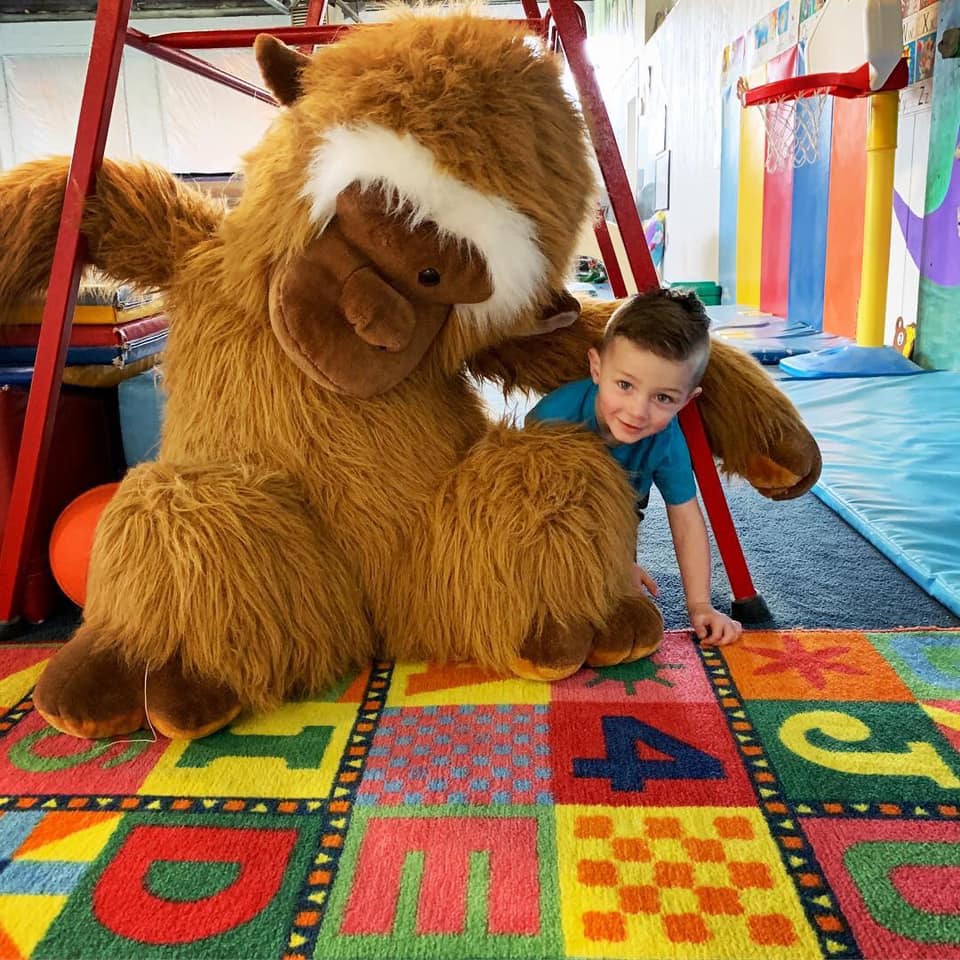 little boy in blue shirt brown hair sitting with a giant stuffed monkey